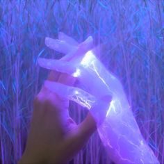 a hand holding something in front of some tall grass with purple light coming through it