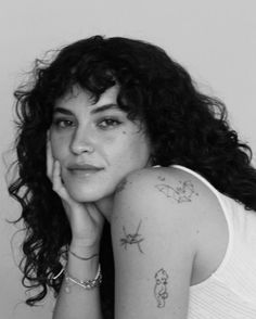 a black and white photo of a woman with tattoos on her arm looking at the camera