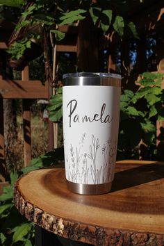 a stainless steel tumbler sitting on top of a wooden table next to some plants