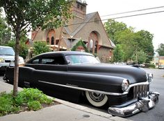 an old black car parked on the side of the road in front of a church