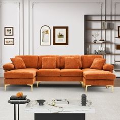 an orange couch sitting in a living room next to a book shelf with pictures on it