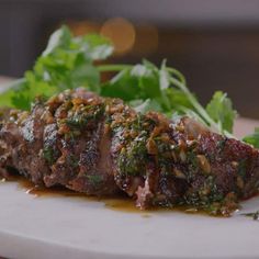 a piece of meat is sitting on a cutting board with some greens and seasoning