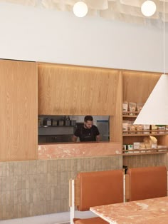 a man working behind the counter in a restaurant with lots of wooden cabinets and chairs