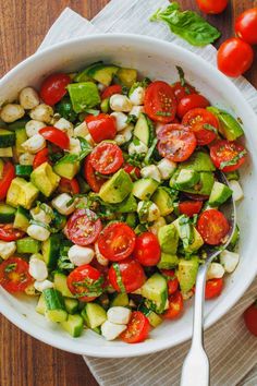 a white bowl filled with cucumber, tomato and chickpeas salad on top of a wooden table