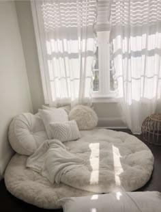 a large round bed in front of a window with white curtains and pillows on it