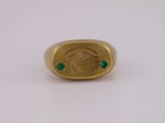 The iconic symbol of the Eye of Horus, revered for its protective powers, is boldly engraved on the cushion signet face. Flanking the eye are two brilliant lab-grown emeralds, reminiscent of the lush beauty of ancient Egypt. This ring is a masterful blend of historic symbolism and modern sophistication, designed with an aged brush finish 22k gold vermeil. Made in solid sterling silver, this ring is a weighty piece. Discover a piece that connects the mystic past with the brilliant present. This piece is made to order, so please allow approximately 3 weeks for the craftsmanship required. Alternative stone options available - please reach out for more info. Instagram - @caeliajewellery Website - www.caeliajewellery.com/ Symbolic Oval Etched Signet Ring, Symbolic Etched Oval Signet Ring, Gold Engraved Emerald Ring Gift, Engraved Gold Emerald Ring As A Gift, Symbolic Oval Engraved Ring For Ceremonial Occasions, Symbolic Etched Signet Ring, Symbolic Oval Etched Rings, Symbolic 14k Stamped Engraved Ring, Symbolic Etched Oval Engraved Ring