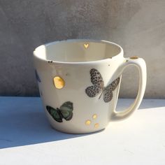 a white coffee cup with butterflies painted on the side and gold dots around the rim