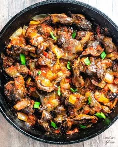 a skillet filled with meat and vegetables on top of a wooden table