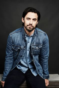 a man sitting on top of a wooden bench wearing a denim shirt and jeans jacket