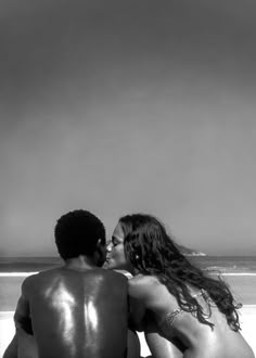 two people sitting on the beach kissing each other