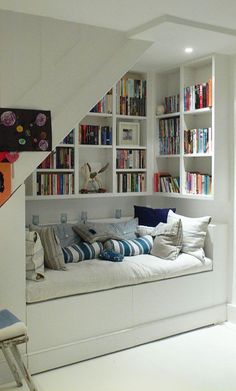 a living room filled with lots of furniture and bookshelves next to a stair case