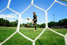 a man kicking a soccer ball in front of a goalie net on a field