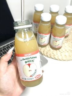 a person is holding a bottle of apple cider in front of a laptop computer