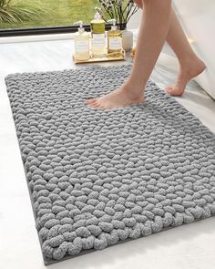 a person walking across a bathroom rug on top of a white floor next to a window