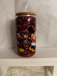 a glass jar with mickey mouse and minnie mouse on it sitting on a white shelf