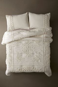 a white bed with two pillows on top of it next to a pillow and blanket