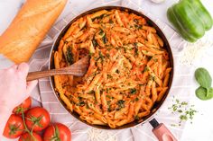 a pan filled with pasta and vegetables on top of a white cloth next to bread