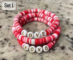 Valentines day bracelets are now here! Snag yours before they are gone. Perfect small gift for friends and family. Beads are placed in a random order and will not be the same pattern as the photo. (same colors will be used: red, pink, light pink and white.) Letters can be changed from black to gold if desired. If not specified then gold letters will be used for set one and black letters will be used for set two. Please specify if you want the bead color different in the personalization box below Valentines Day Bracelets, Bracelet Ideas Clay Beads, Valentines Day Clay, Small Gift For Friends, Small Gifts For Friends, Gifts For Valentines, Clay Bead Bracelets, Valentines Bracelets, Disc Bracelet