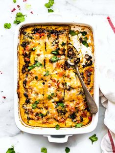 an enchilada casserole in a white dish with a serving spoon