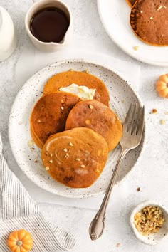 three pancakes on a white plate with butter and pumpkins in the background, next to a cup of coffee