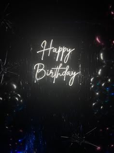 happy birthday neon sign surrounded by balloons and confetti on black background with white writing