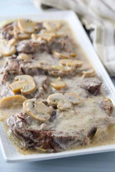 a white plate topped with meat covered in gravy next to sliced bananas and mushrooms