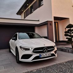 a white mercedes cla is parked in front of a house with two garage doors