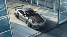 a silver sports car is parked in front of a glass building with its doors open