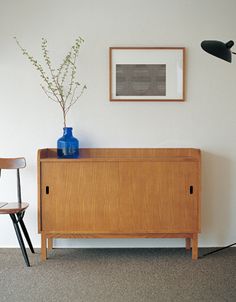 a wooden cabinet sitting next to a black lamp and a blue vase on top of it