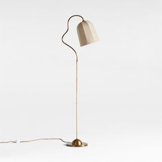 a floor lamp with a white shade on the top and a gold base, sitting against a white background