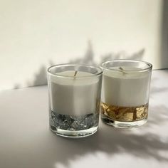 two candles sitting next to each other on top of a white table with water in it