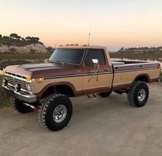 a brown and tan truck parked on top of a dirt road next to a body of water