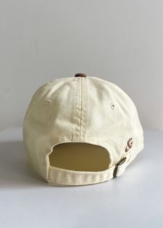 a white baseball cap with a brown leather patch on the front and back side, sitting on a white surface