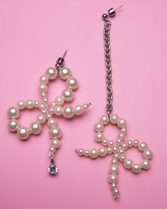 two pairs of earrings with pearls hanging from them on a pink surface, one is shaped like a snowflake and the other is shaped like a cross