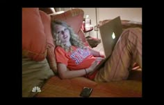 a woman sitting on a couch with a laptop computer in her lap and looking at the camera