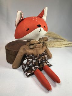 a stuffed fox is sitting on top of a hat box and wearing a brown dress