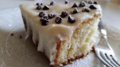 a piece of cake with white frosting and chocolate chips on top sits on a plate next to a fork