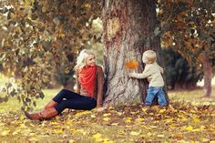 a woman sitting next to a tree with a little boy on her lap looking at it