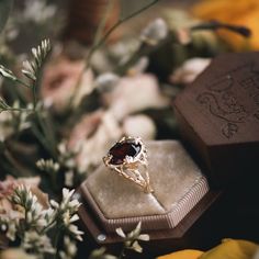 a close up of a ring on a box with flowers in the background and other items around it