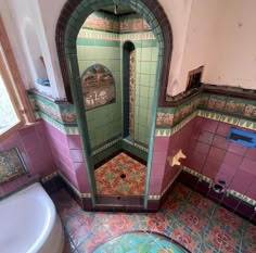 an old bathroom with pink and green tiles on the walls, toilet and bathtub