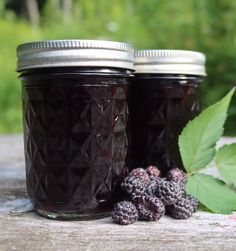 two jars filled with blackberry jam next to some berries