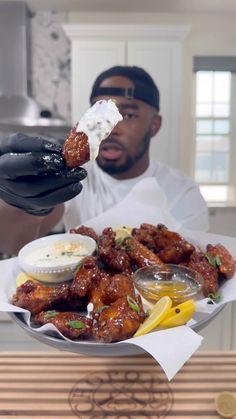 a man in black gloves is holding up a plate with wings and dips on it