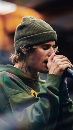 a young man in a green jacket and beanie singing into a microphone