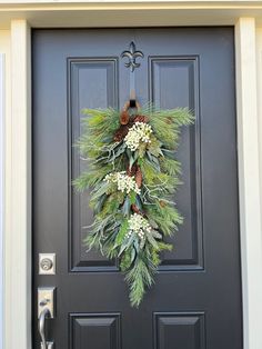 a wreath on the front door of a house with pine cones and white flowers hanging from it