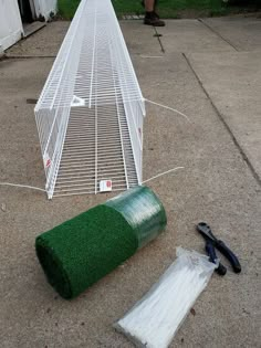 a large white bird cage sitting on top of a sidewalk next to a roll of grass