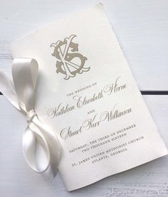 a wedding card with a ribbon tied around it on top of a white wooden table