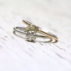 two gold and silver wedding rings with a diamond in the center on a white wooden surface