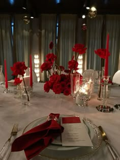 the table is set with silverware and red flowers in vases, candles, and napkins