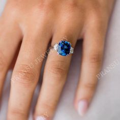 a woman's hand with a blue ring on top of her finger and an oval shaped diamond in the middle