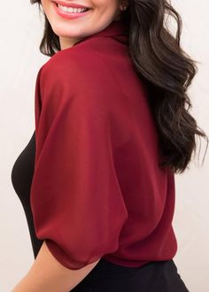 a woman with long dark hair wearing a red blouse and black pants smiling at the camera